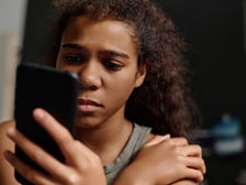 Teenage girl looks at her phone dejectedly like she's just been rejected