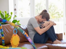 An unhappy mother dealing with parental burnout sitting on a couch in front of a child's play set
