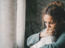 A sad and worried mother holding a pillow looking out the window feeling guilty