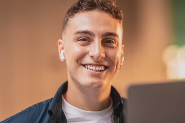 Young adult male smiling at the camera with earbuds in