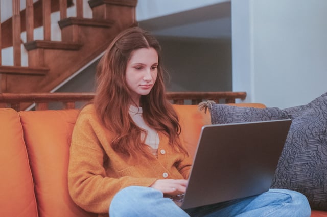 Youn teen on her laptop sitting on an orange couch