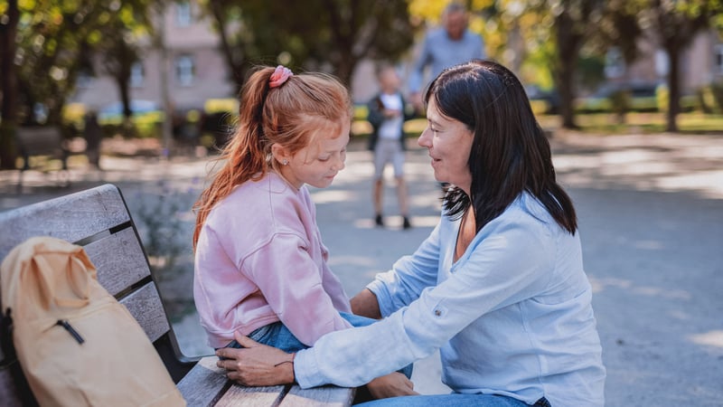 Kid dealing with anxiety while talking to her mom on a park bench