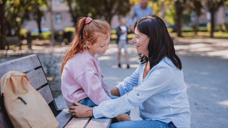 Kid dealing with anxiety while talking to her mom on a park bench