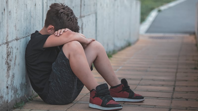 Kid sitting against wall crying from bullying