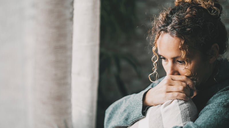 A sad and worried mother holding a pillow looking out the window feeling guilty