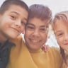 three children smiling at the camera while hugging each other