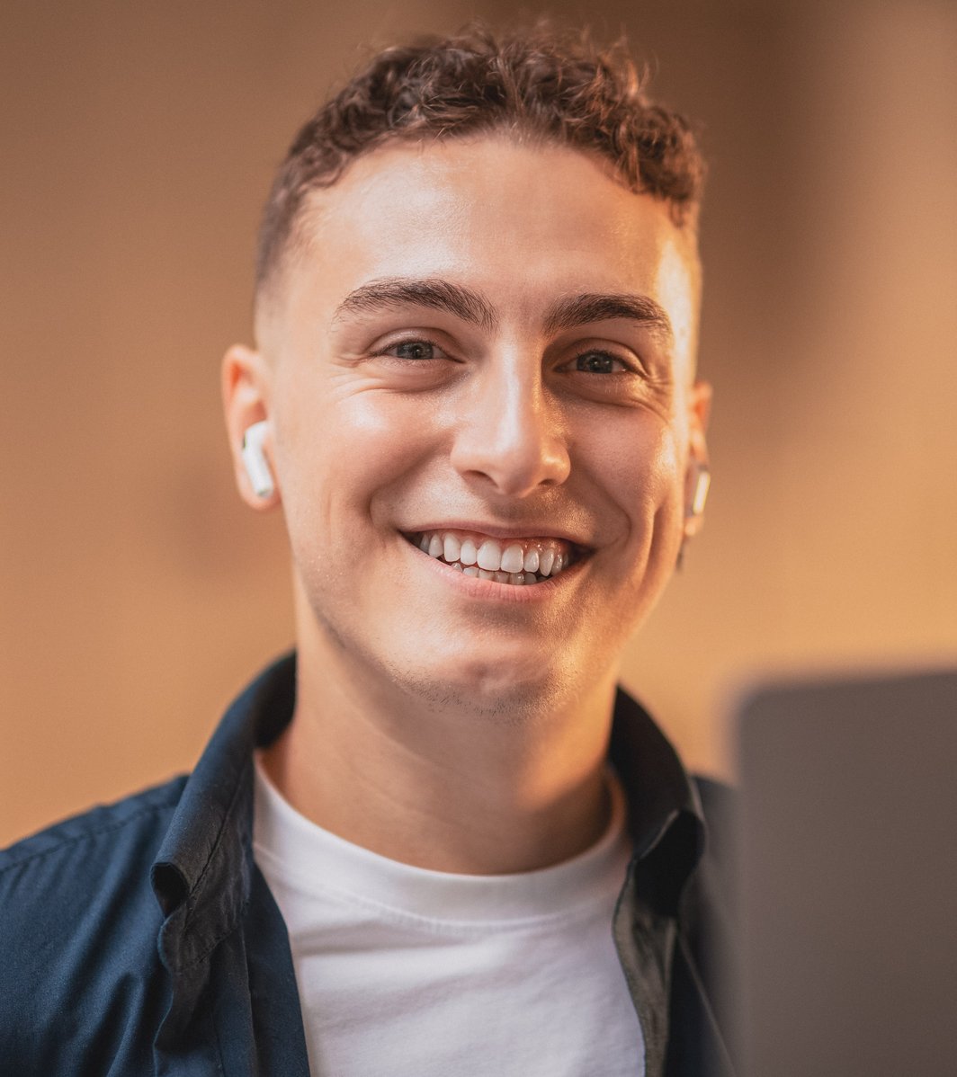 Young adult male smiling at the camera with earbuds in