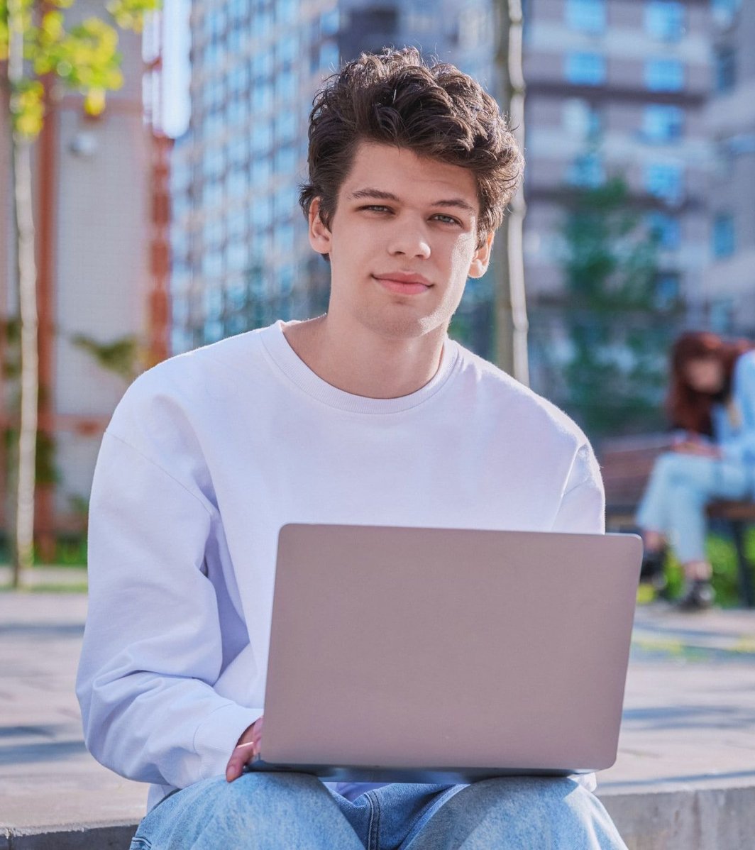 Young adult male in white shirt on a laptop outside