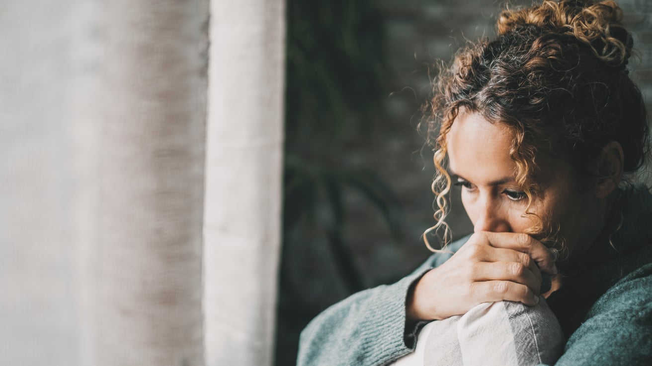 A sad and worried mother holding a pillow looking out the window feeling guilty