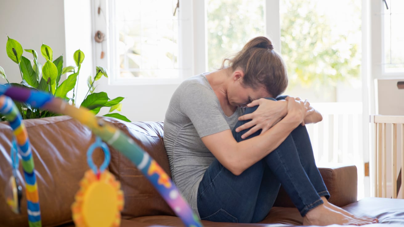 An unhappy mother dealing with parental burnout sitting on a couch in front of a child's play set