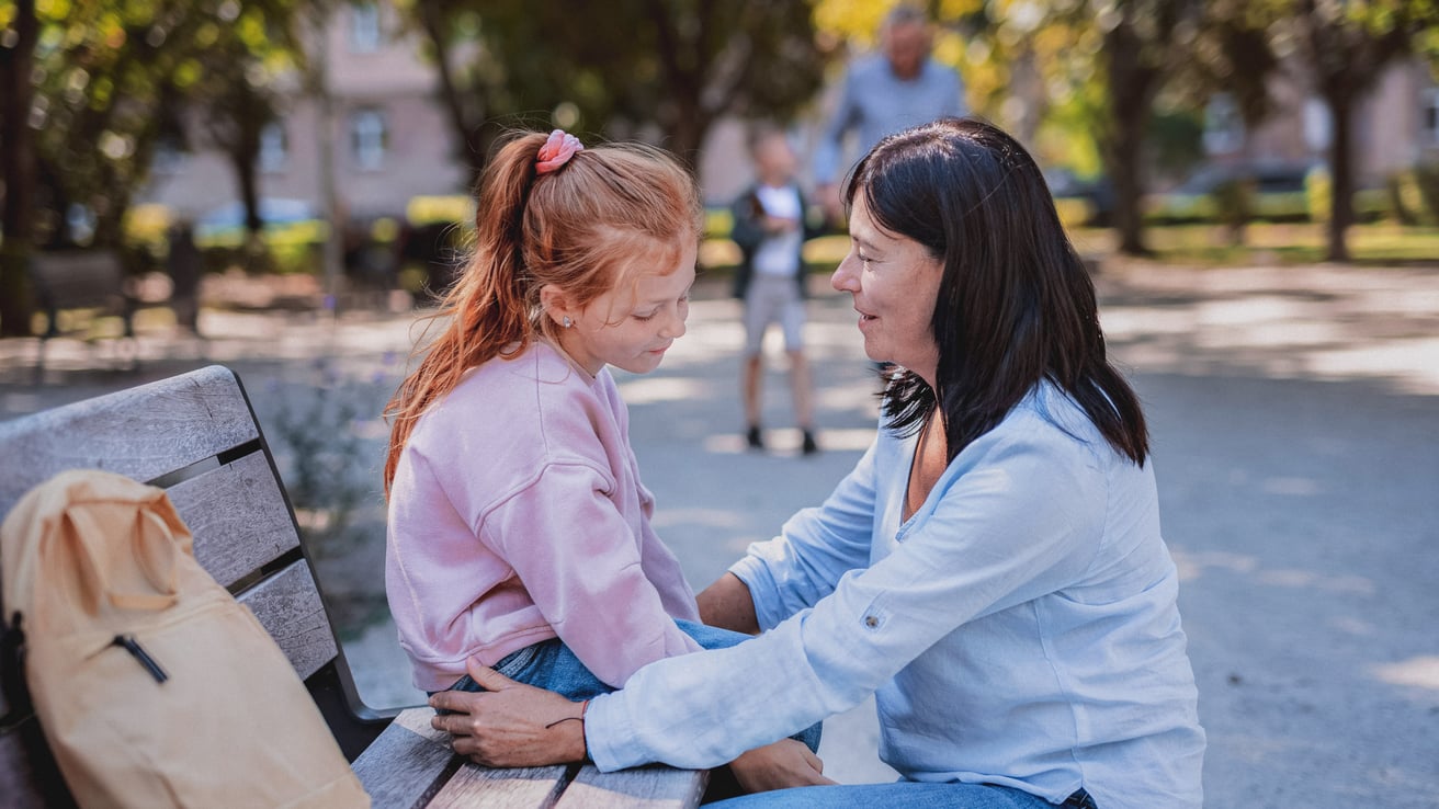 Kid dealing with anxiety while talking to her mom on a park bench