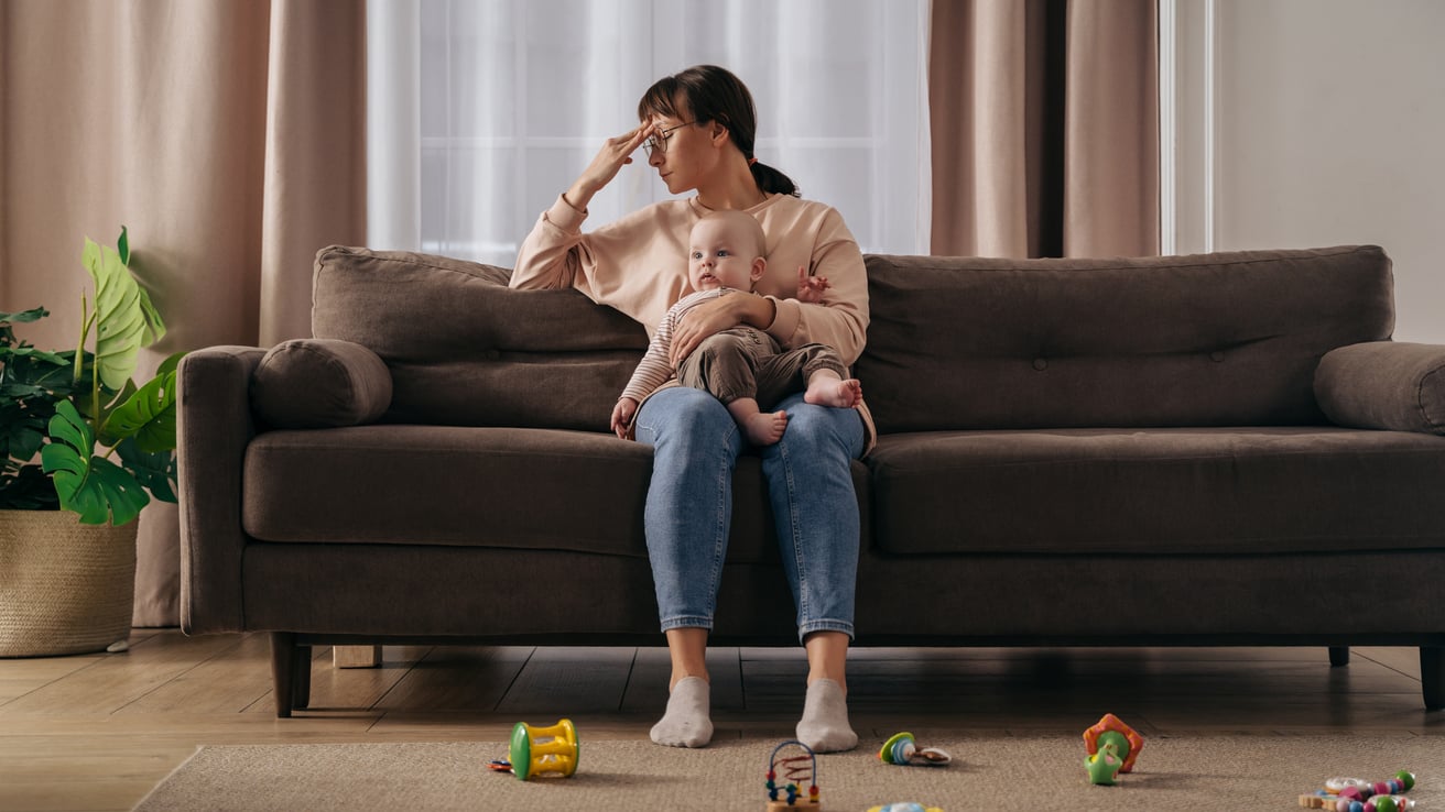 Mother experiencing stay-at-home-mom depression sitting on a couch holding a baby