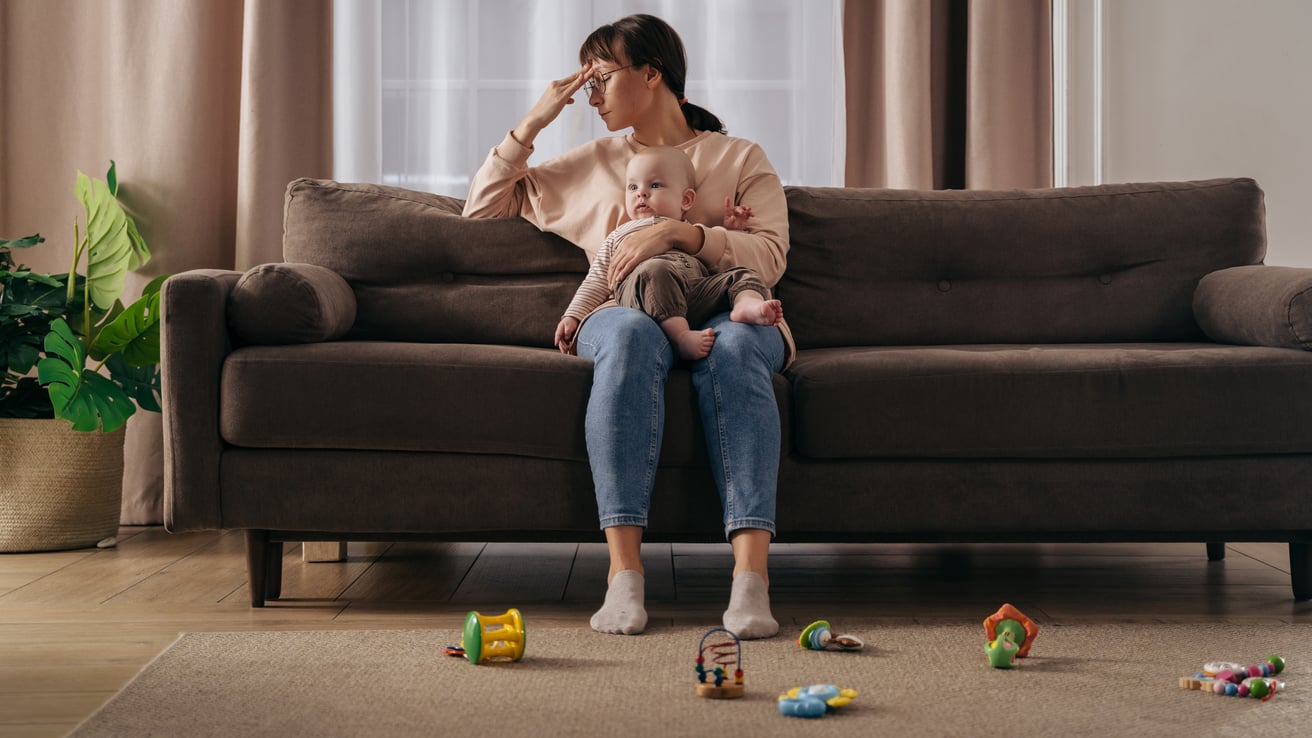 Mother experiencing stay-at-home-mom depression sitting on a couch holding a baby