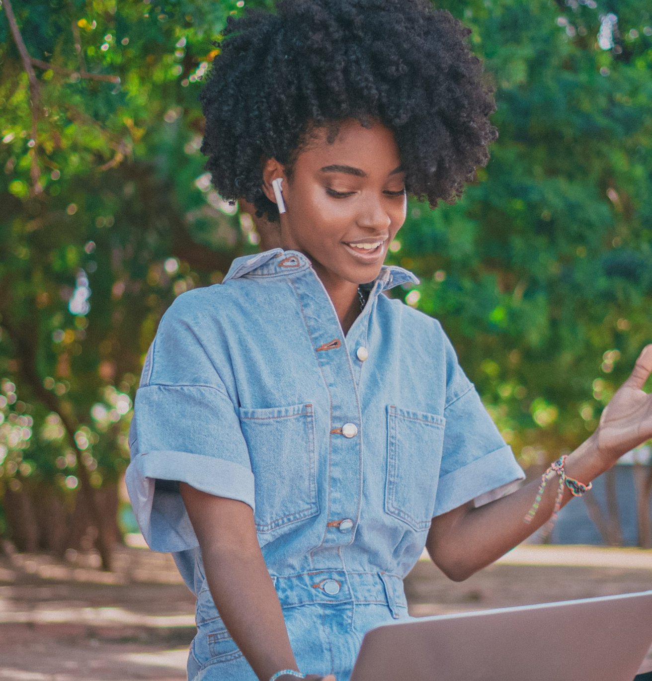 Young adult female with dark skin and a jean jacket at her laptop outside