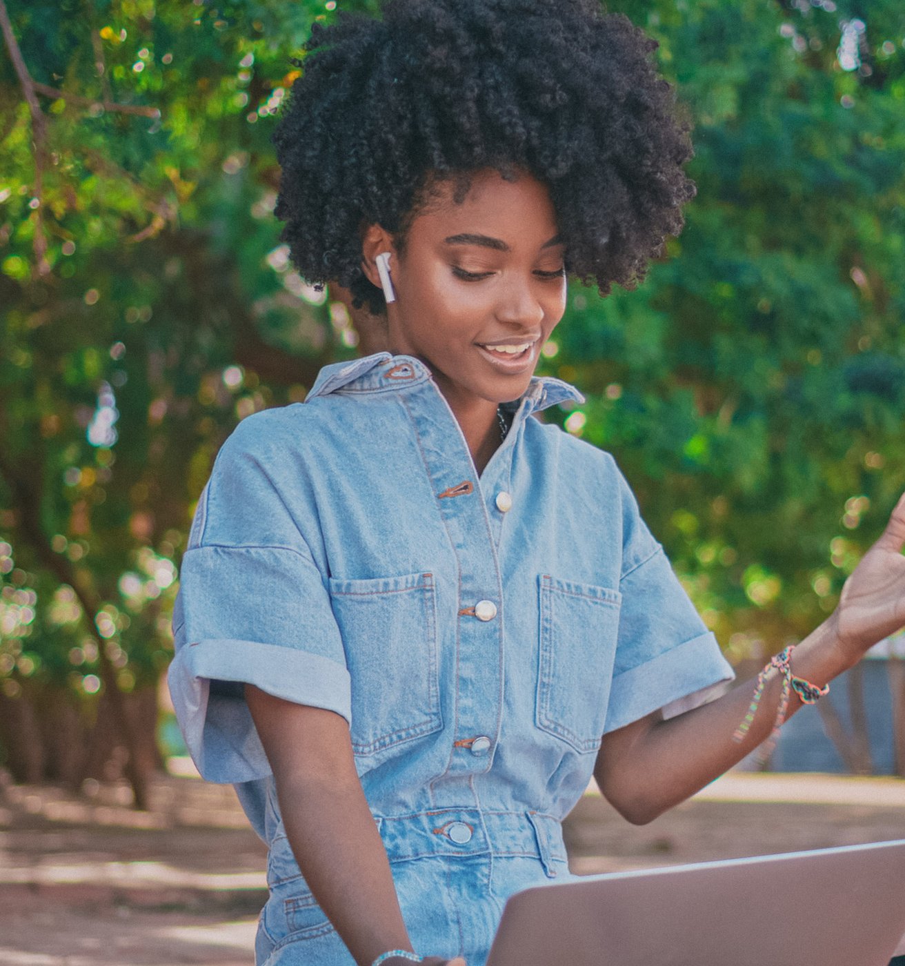Young adult female with dark skin and a jean jacket at her laptop outside