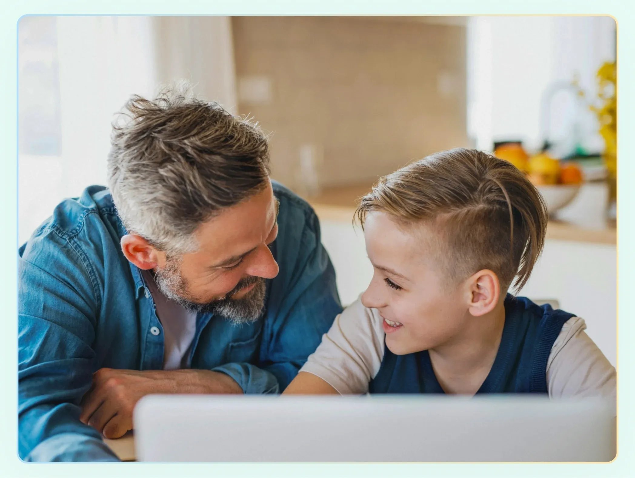 Dad and son in the kitchen smiling at each other with computer in front of them