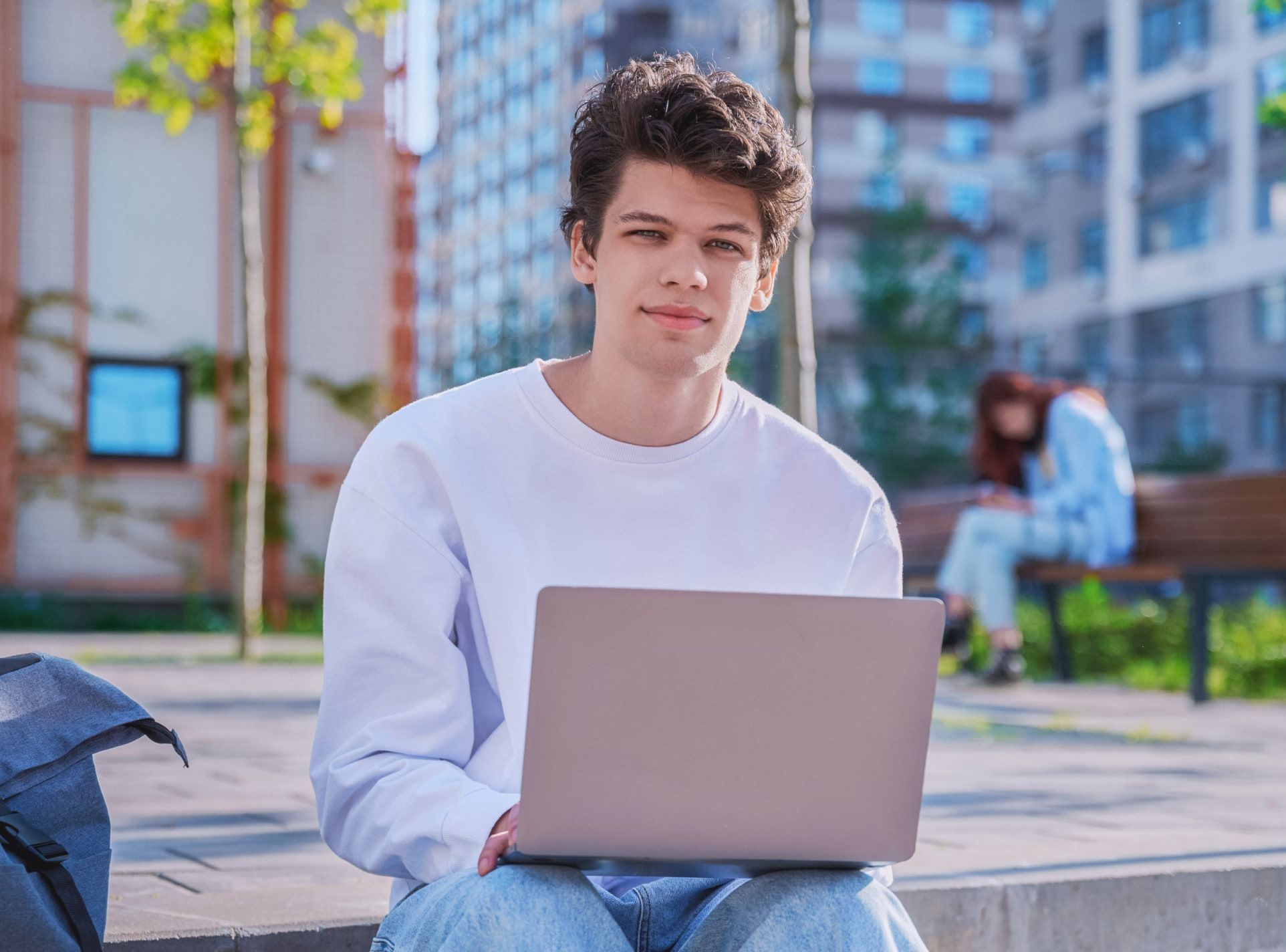 Young adult male in white shirt on a laptop outside