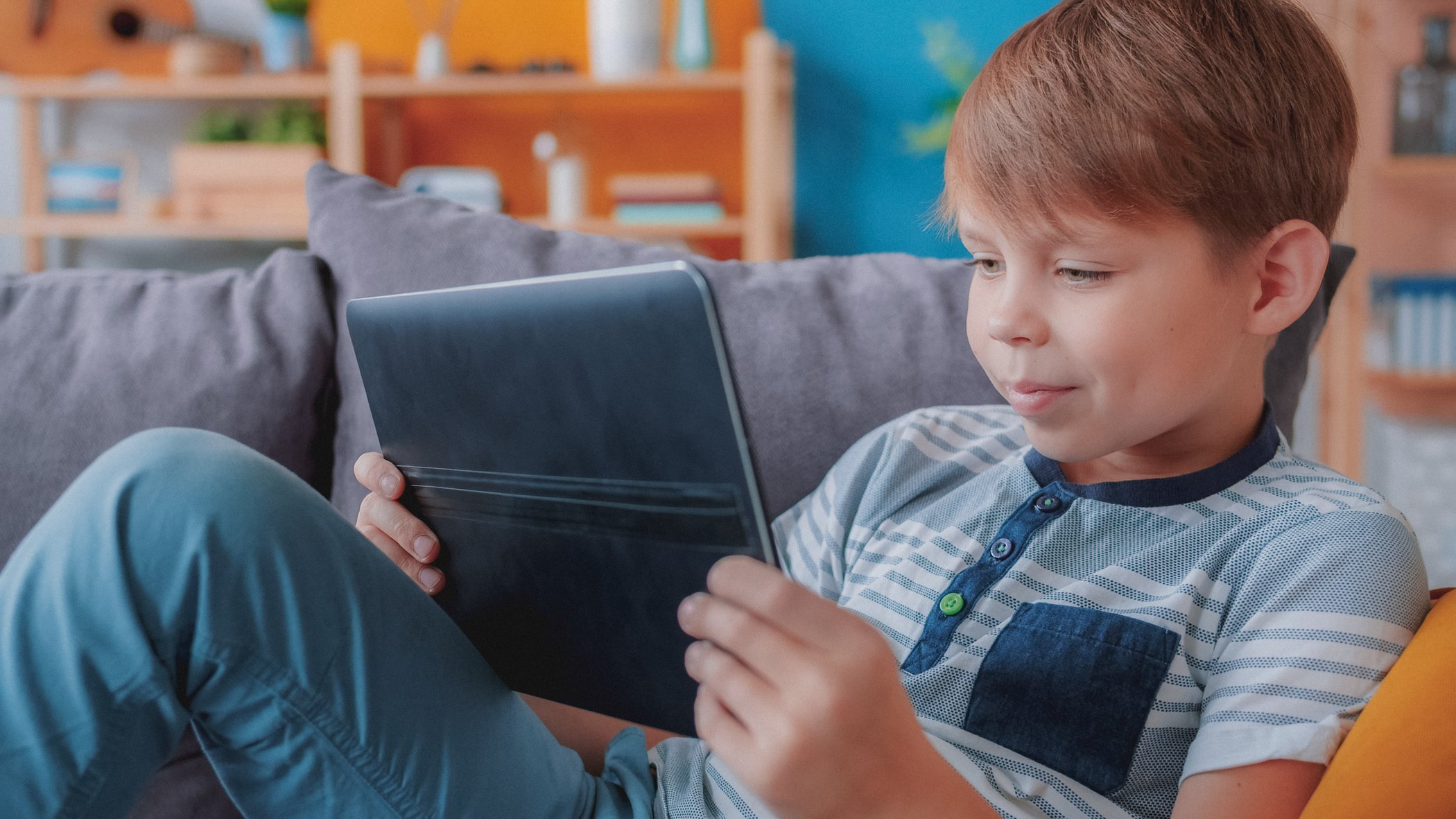 young boy sitting on the couch looking at his ipad