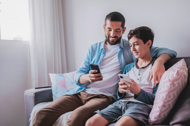 dad and son sitting on the couch smiling at phone together