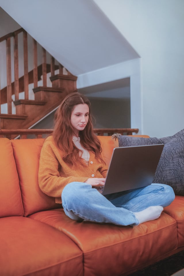 Youn teen on her laptop sitting on an orange couch
