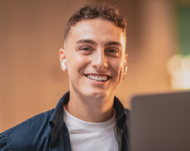 Young adult male smiling at the camera with earbuds in