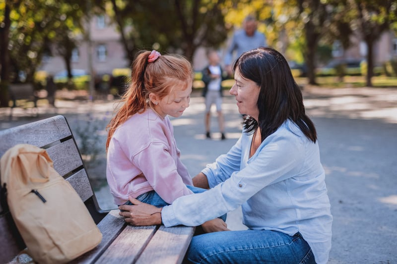 Kid dealing with anxiety while talking to her mom on a park bench