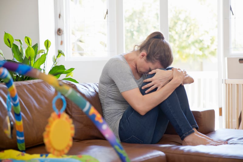 An unhappy mother dealing with parental burnout sitting on a couch in front of a child's play set