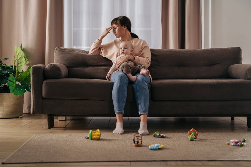 Mother experiencing stay-at-home-mom depression sitting on a couch holding a baby