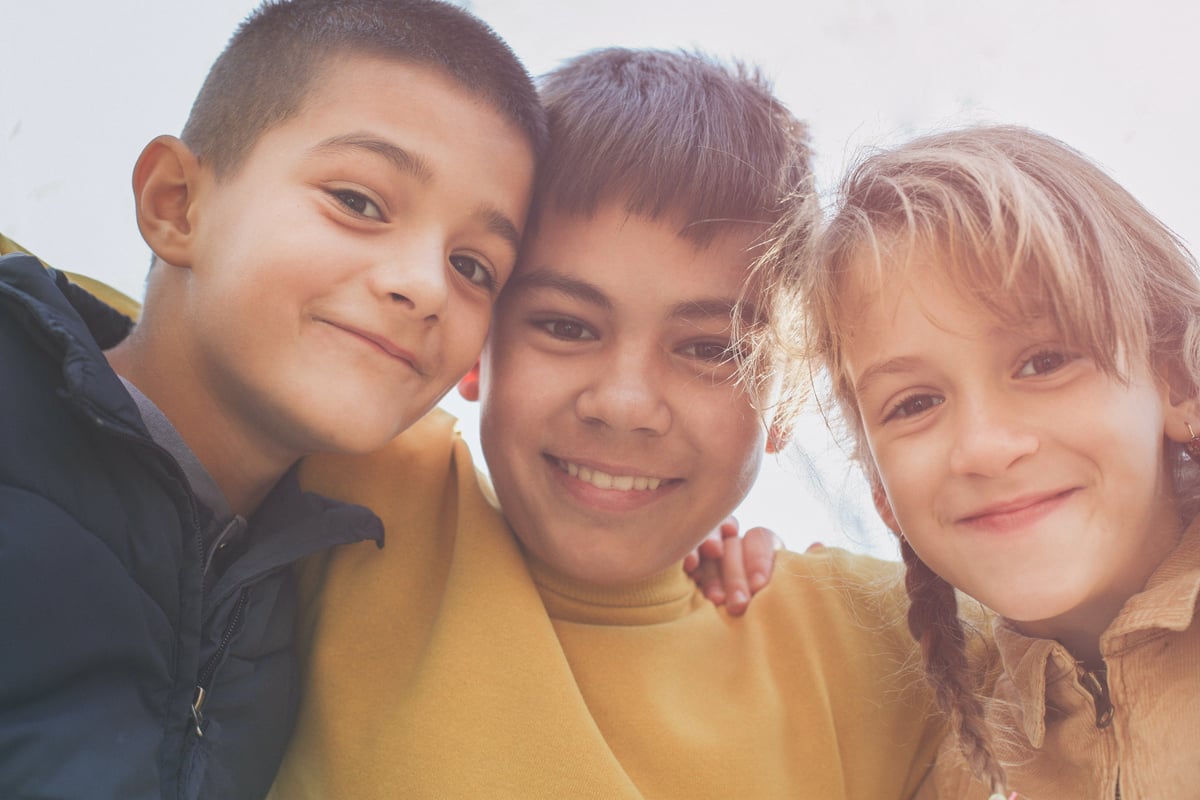 three children smiling at the camera while hugging each other