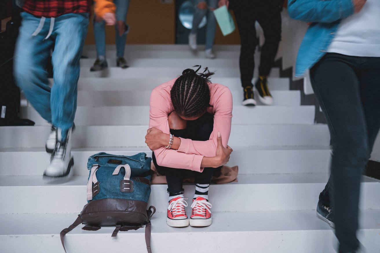 Teen girl sitting on stairs with head in her legs suffering from PTSD