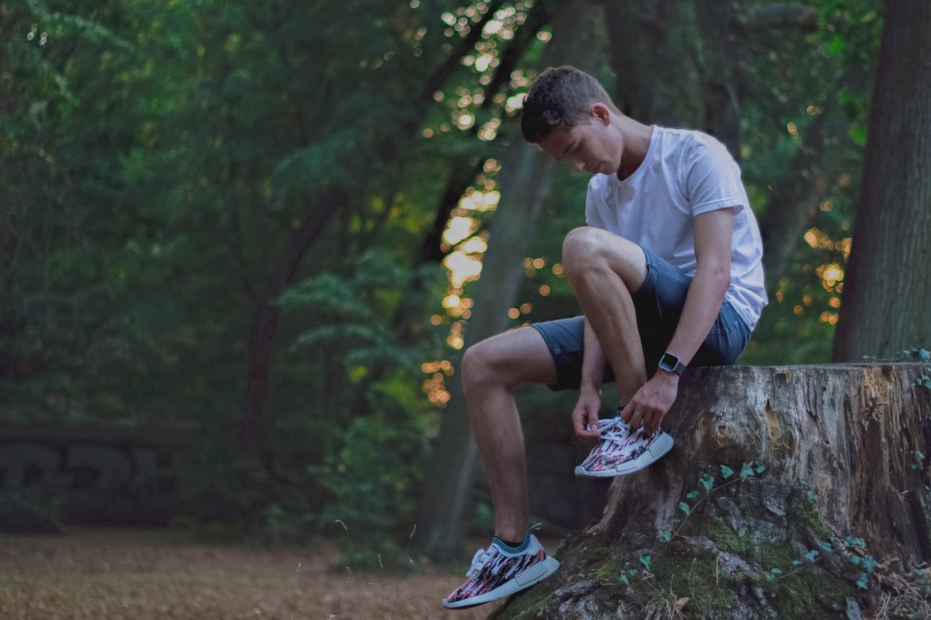 Teen sitting on a tree stump tying his shoes