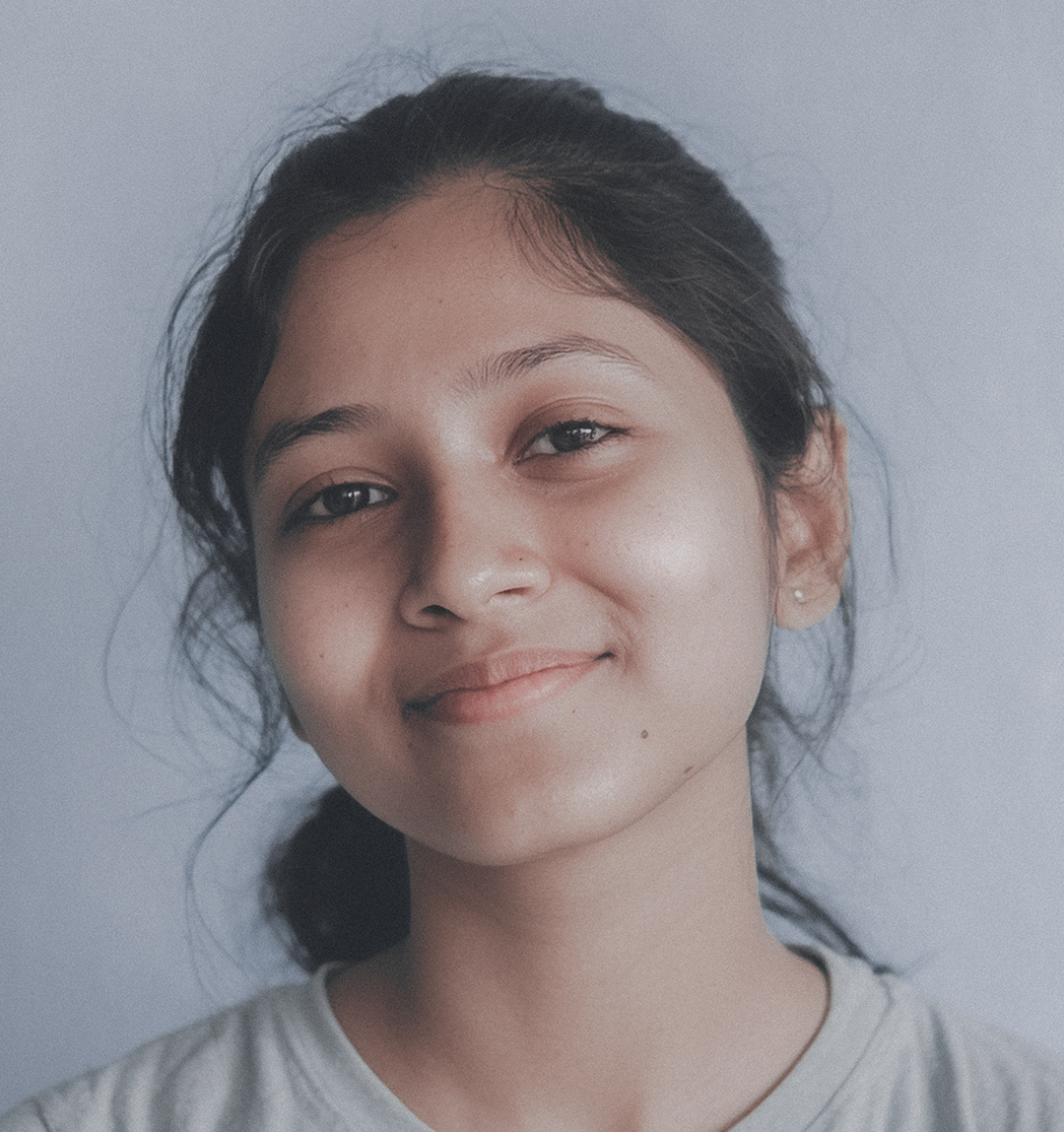 A young teenage girl with dark hair pulled back smiles gently at the camera. She appears calm and approachable in this headshot against a plain background.