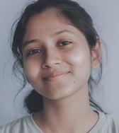 A smiling teenage girl of South Asian descent looks directly at the camera in a close-up portrait, conveying a calm and approachable mood.