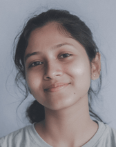 A young teenager with dark hair pulled back smiles gently at the viewer, against a light, plain background. Her expression is calm and approachable.