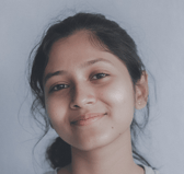 A portrait of a smiling teen of South Asian descent looking directly at the viewer with a calm and welcoming expression. The background is plain and light-colored.
