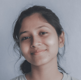 A close-up portrait of a smiling young woman with dark hair pulled back. She looks directly at the camera with a gentle, approachable expression against a plain, light-colored background.