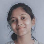 A teen with dark hair and a gentle smile looks directly at the camera, posing for a close-up portrait against a plain, light background.