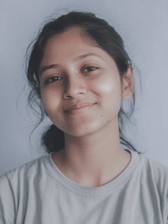A portrait of a young South Asian female teenager looking directly at the camera with a soft, friendly smile against a plain, light-colored background.
