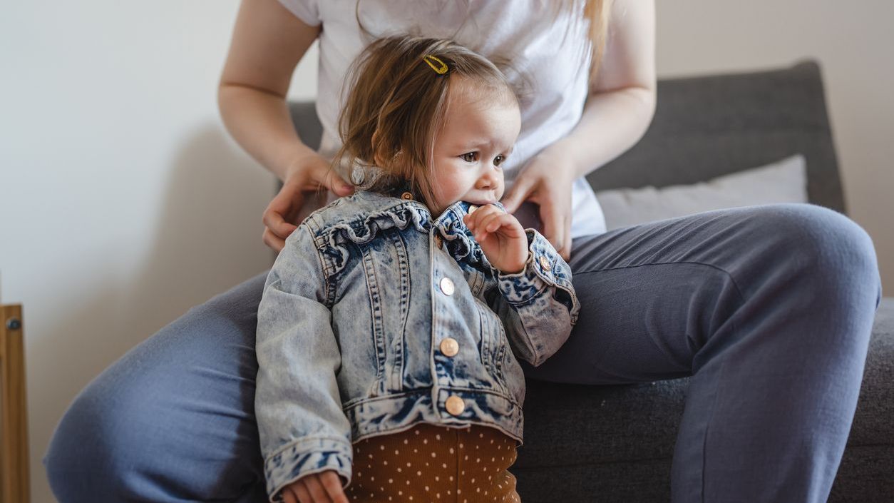 kid chewing jacket with parent sitting behind her